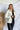 Front view of model wearing the Yosemite Puffer Jacket that has ivory puffer fabric, two front pockets, black zipper details, a zip-up front, and a hood. Worn over black top.