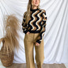 Full body front view of model wearing the Love Sick Sweater that has black, brown and cream knit fabric with a swirl pattern, a cropped waist, a round neckline, long balloon sleeves, and black ribbed trim