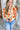 Close front view of model wearing the Happy With You Cardigan that has beige knit fabric, a dark orange and light orange flower pattern, a cropped waist, tortoise buttons, and long sleeves with beige ribbed wrists