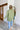 Back view of model wearing the Check It Out Top that has olive satin fabric with a monochromatic checkered pattern, two front chest pockets, a button up front with a collar, and long sleeves.