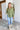 Full body front view of model wearing the Check It Out Top that has olive satin fabric with a monochromatic checkered pattern, two front chest pockets, a button up front with a collar, and long sleeves.