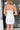 Back view of model wearing the Ice Queen Dress that has white fabric with a metallic silver floral pattern, a strapless neckline with pleated ruffle detailing, a lining, and a back zipper closure