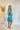 Side view of model wearing the Downtown Plans Dress which features light teal, sheen, satin fabric; square neckline, smocked back details and 3/4 sleeves with elastic and ruffle wrists.