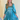 Front view of model wearing the Downtown Plans Dress which features light teal, sheen, satin fabric; square neckline, smocked back details and 3/4 sleeves with elastic and ruffle wrists.