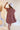 Back view of model wearing the Look At You Satin Dress that has terracotta satin fabric, two front chest pockets, v-neckline and cuffed short sleeves