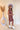 Full body side view of model wearing the Look At You Satin Dress that has terracotta satin fabric, two front chest pockets, v-neckline and cuffed short sleeves