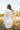 Back view of model wearing the Heading West Dress, that has ribbed cream fabric, fitted long sleeves, a mock neck, ruching on one side, and a cream lining