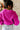 Back view of model wearing The Magenta Haze Sweater features a magenta pink colored knit material, an oversized collar, a V neckline, long cuffed sleeves, and a thick bottom hem.