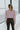 Back view of the One Thing Bodysuit that features a dark mauve color, a surplice neckline, a puffy sheer long sleeve, a bikini bottom, and a snap closure.