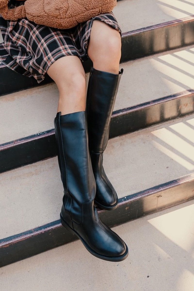 Close up view of model wearing the Pennie Tall Riding Boot in Black which features round-toe pull-on style with inner ankle zipper closure, pull tabs on each side, cushioned insole and memory foam for added comfort.