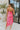 Back view of the Pink Dreams Dress that features a monochromatic pink houndstooth pattern, a cowl neckline, a sleeveless design with thin adjustable straps, and a side slit.