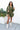 Full body front view of model wearing the One Way Ticket Romper, that features olive fabric, wood button closures, v neckline, two front pockets with tie details and balloon long sleeves with elastic wrists