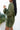 Side view of model wearing the One Way Ticket Romper, that features olive fabric, wood button closures, v neckline, two front pockets with tie details and balloon long sleeves with elastic wrists