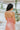 Back view of the Coastal Crush Dress that features a coral colored material, a cowl neckline, a sleeveless design with thin adjustable straps, a side slit, and a midi length.
