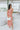 Frontal view of the Coastal Crush Dress that features a coral colored material, a cowl neckline, a sleeveless design with thin adjustable straps, a side slit, and a midi length.