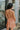 Back view of the Something Like That Dress that features a salmon satin material, a cowl neckline with cups at the bust, a sleeveless design with thin adjustable straps, a waist cut-out, an elastic waistline, and a criss-cross strap back.