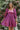 Frontal view of the Wanderlust Dress that features a wine colored silk material, a straight neckline, a puffy half sleeve, a smocked back, and a mini length.