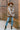 Full body view of model wearing the Twist Of Fate Cardigan which features brown and cream knit fabric, checkered pattern, tortoise button up front closure, v neckline, brown ribbed knit fabric outline and long balloon sleeves with brown ribbed knit wrists