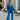 Full body view of model wearing the Be You Pants which features royal blue pleated fabric, elastic waistband and flare pant with lettuce detail on the hem.