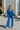 Full body view of model wearing the Be You Pants which features royal blue pleated fabric, elastic waistband and flare pant with lettuce detail on the hem.