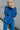 Back view of model wearing the Be You Pants which features royal blue pleated fabric, elastic waistband and flare pant with lettuce detail on the hem.