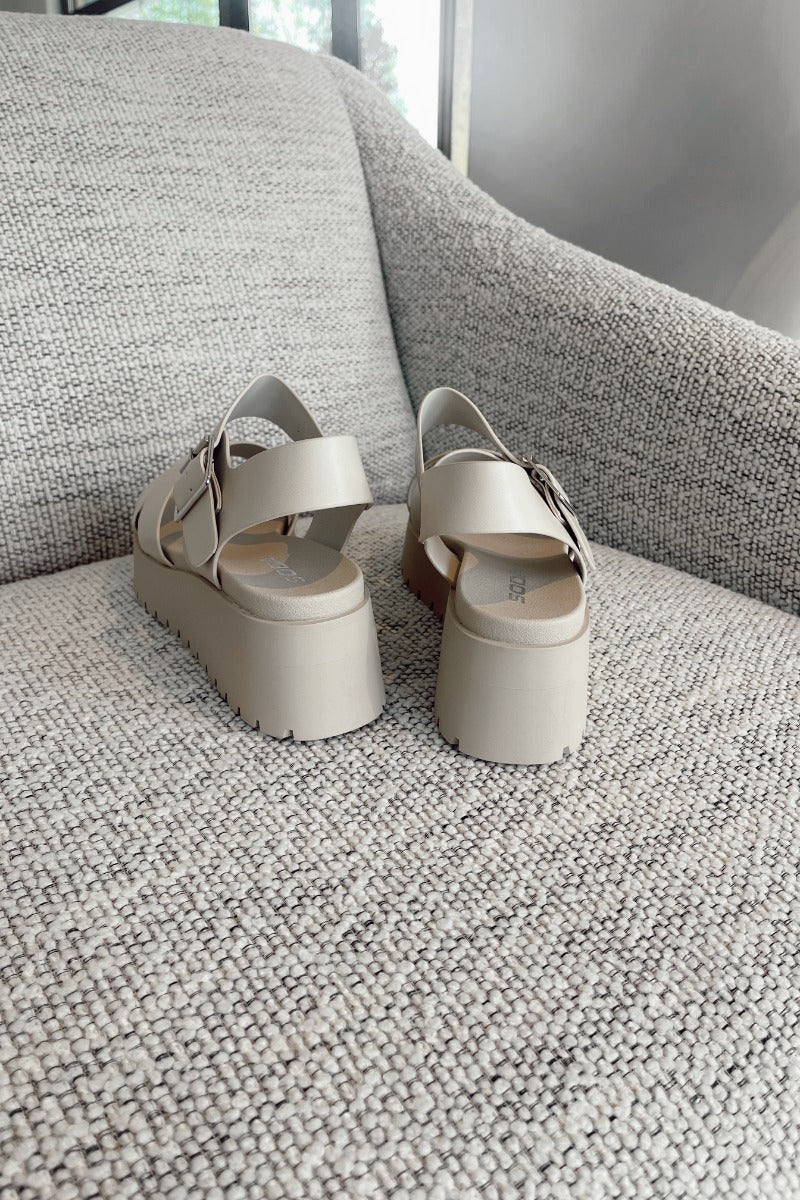 Heel view of the Alyssa Platform Sandals which features an off-white leather fabric, platform sole, upper thick straps and adjustable with ankle strap and silver buckle design.