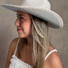 Side view of model wearing the Westside Ivory Cowgirl Hat which features cowboy shape, ivory suede fabric and rhinestone design on bottom of hat.