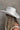 Back side view of model wearing the Westside Ivory Cowgirl Hat which features cowboy shape, ivory suede fabric and rhinestone design on bottom of hat.