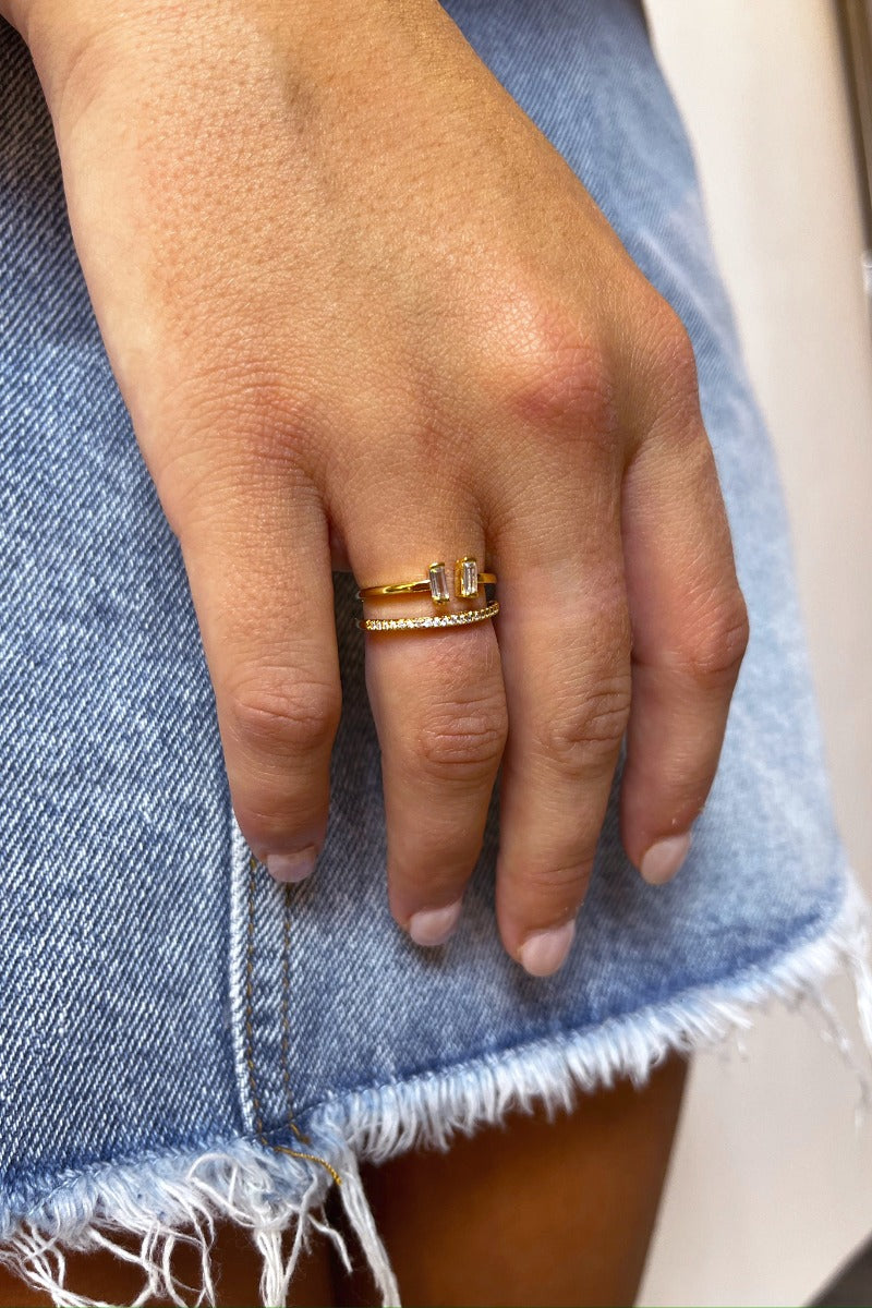Close up view of model wearing the Double The Trouble Ring which features two-layered gold ring bands with clear stones and separated band with emerald shaped clear stones.