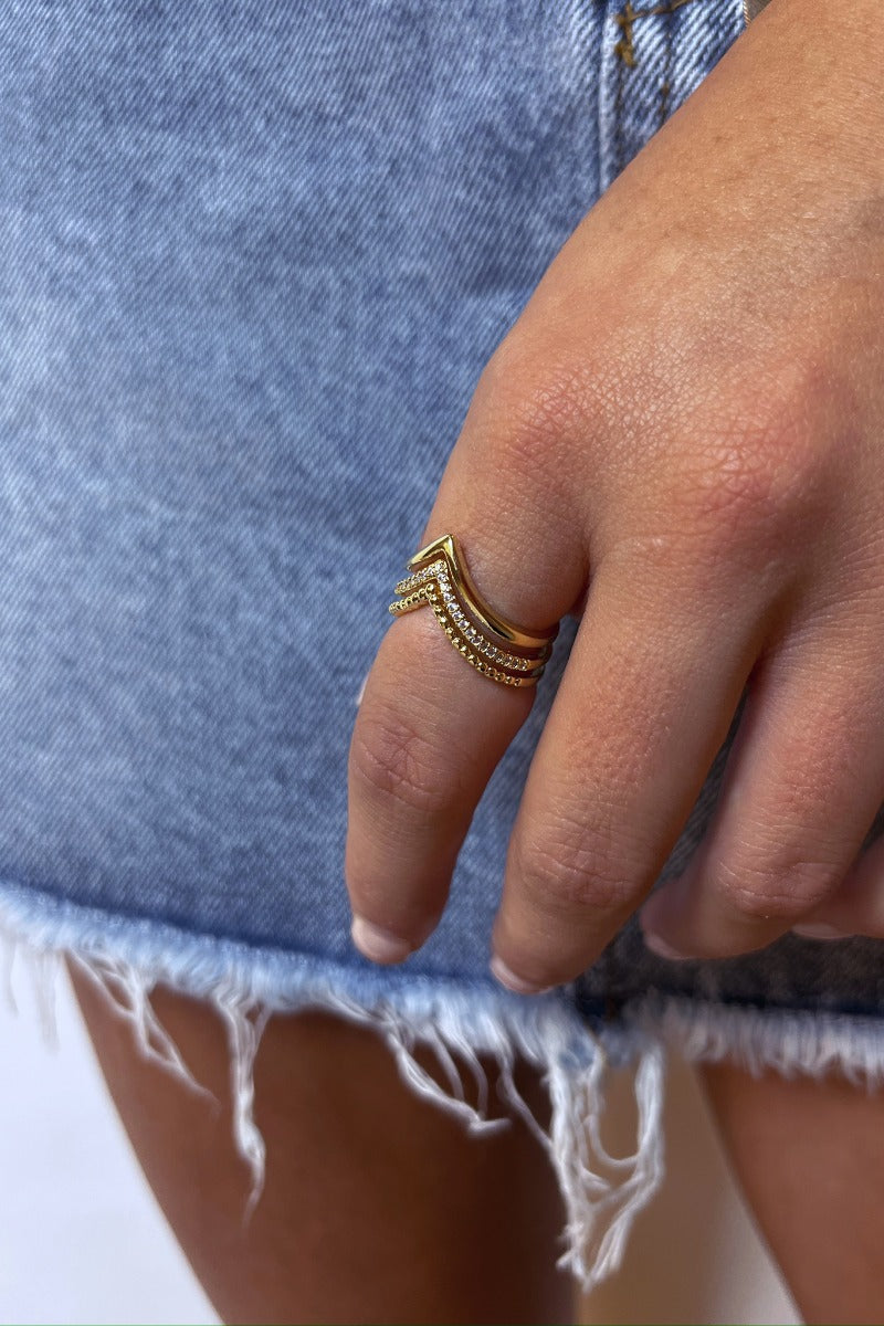 Close up view of model wearing the Wishful Thinking Ring which features three-layered gold ring bands chevron shaped with clear stones and bead details.