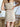 Close back view of model wearing the Desert Sands Skirt that has natural colored fabric, an open knit crochet design, natural colored lining, mini length, and a drawstring tie with tassel details at the waistband