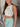 Side view of model wearing the Forever Floral Open-Back Tank that has ivory knit fabric with a blue, green, pink and yellow floral pattern, a cropped waist, a round neck, and an open key hole back with a tie closure.