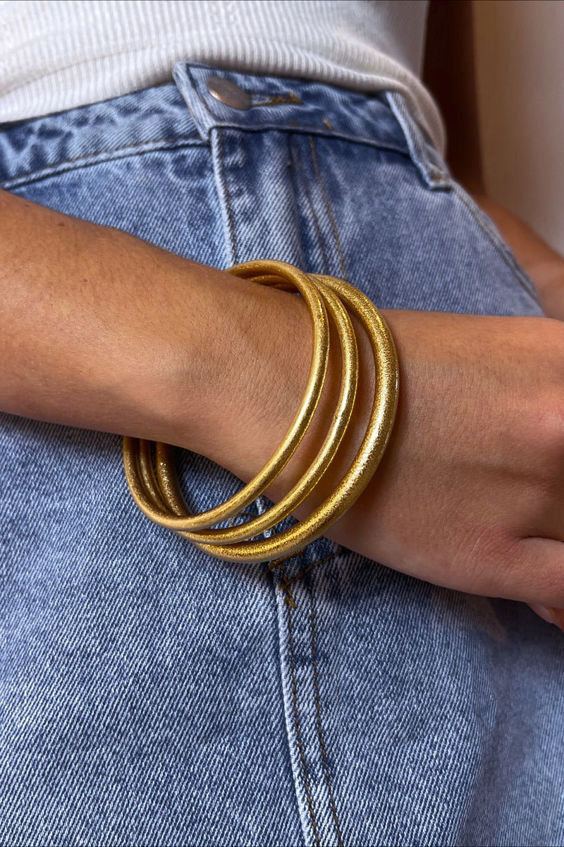Front view of  model wearing the More Than A Dream Bracelet in Gold which features one, gold shimmer metal, thick bracelet. Bracelet is paired with two other bracelets.