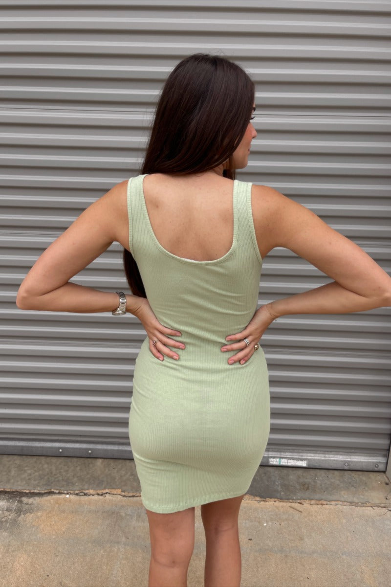 Back view of model wearing the Remember Me Mini Dress which features light sage ribbed fabric, mini length, a round neckline, and thick straps.