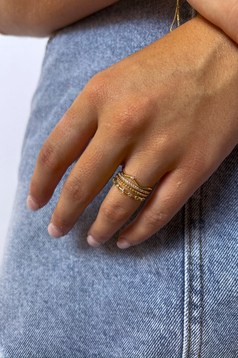 Close up view of model wearing the Wanderlust Ring which features four-layered gold ring bands, one band has circular clear stones, second band is gold beads, third band is covered with mini clear stones and fourth band is wavy with a singular clear stone
