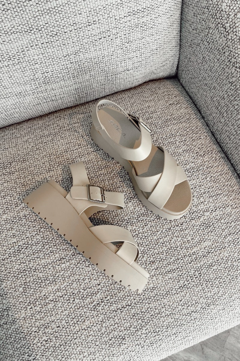 Ariel view of the Alyssa Platform Sandals which features an off-white leather fabric, platform sole, upper thick straps and adjustable with ankle strap and silver buckle design.