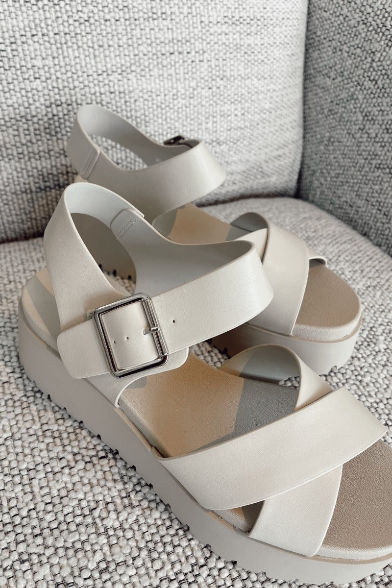 Close up view of the Alyssa Platform Sandals which features an off-white leather fabric, platform sole, upper thick straps and adjustable with ankle strap and silver buckle design.