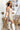 Full side view of model wearing the Desert Sands Skirt that has natural colored fabric, an open knit crochet design, natural colored lining, mini length, and a drawstring tie with tassel details at the waistband