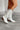 Side view of model wearing the Zane Rhinestone Cowgirl Boot in White which features a western style pattern with rhinestone details, tall boot, pull tabs, monochromatic heel and chic pointed toe.