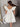 Back view of model wearing the Sweet Life Bubble Dress that features ivory satin fabric, mini length, a bubble hem, a round neckline, ruffle straps and a monochromatic back zipper with a hook closure.