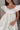 Close front view of model wearing the Sweet Life Bubble Dress that features ivory satin fabric, mini length, a bubble hem, a round neckline, ruffle straps and a monochromatic back zipper with a hook closure.