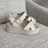 Side view of the Alyssa Platform Sandals which features an off-white leather fabric, platform sole, upper thick straps and adjustable with ankle strap and silver buckle design.