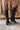 Back view of model wearing the Zane Rhinestone Cowgirl Boot in Black which features a western style pattern with rhinestone details, tall boot, pull tabs, monochromatic heel and chic pointed toe.